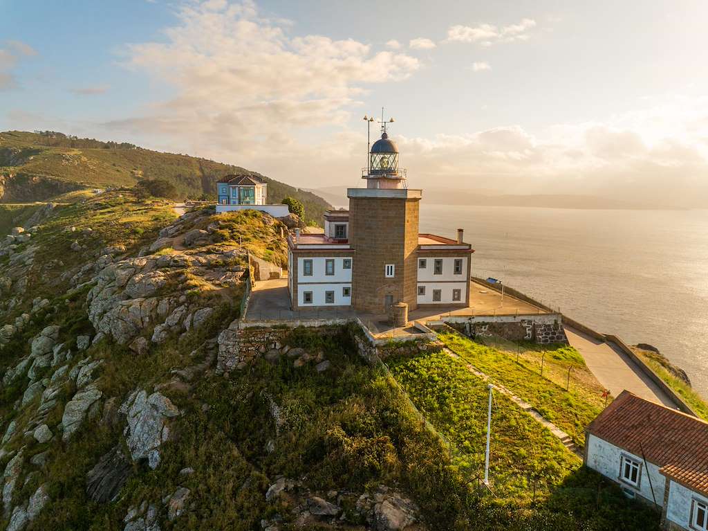 Faro de Finisterre al atardecer con persona contemplando la puesta de sol sobre el Atlántico